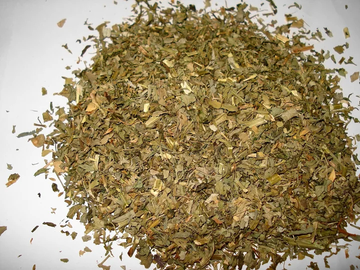 Grămadă de frunze uscate și mărunțite de schinduf, verzui-brune, pe fond alb
