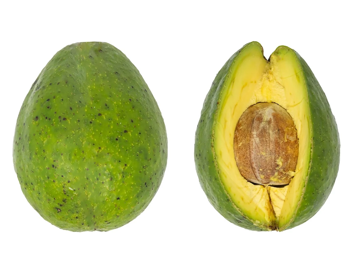 Un avocado întreg și unul tăiat în două, cu pulpa galben-verzuie și sâmburele maro, pe fundal alb