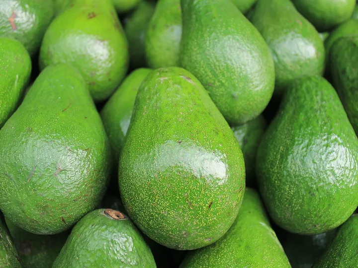 Fructe de avocado în formă de pară, cu coaja verde și lucioasă, îngrămădite unele peste altele