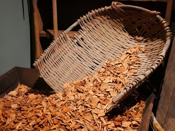 Coș de nuiele răsturnat peste un morman de așchii de lemn portocalii, într-un model de colibă de distilare a camforului