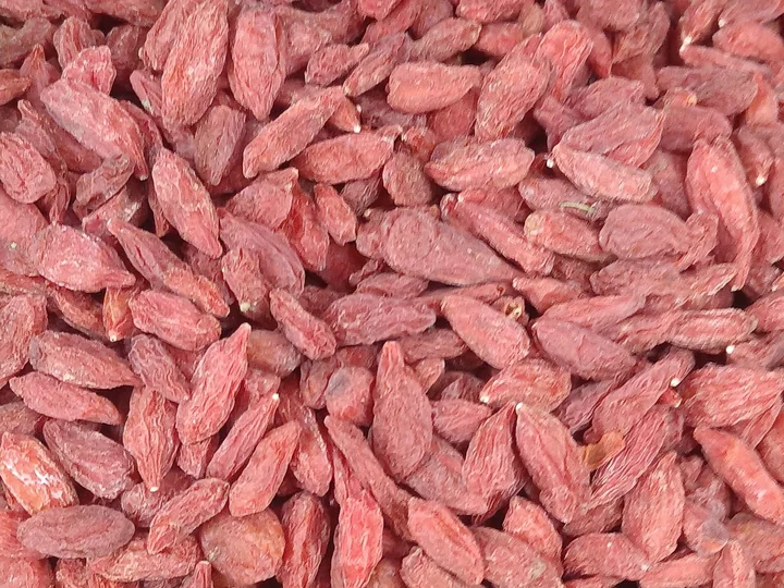 Grămadă de fructe uscate de goji, alungite și zbârcite, roșii-roz, văzute de aproape