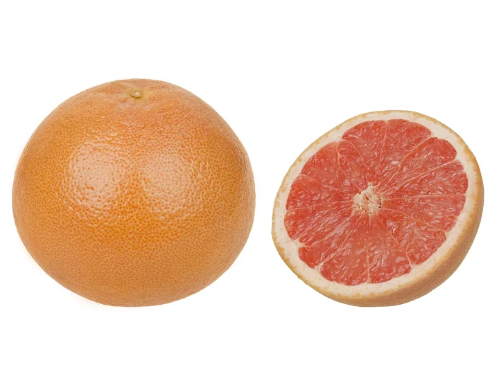Un grapefruit întreg, cu coaja portocalie, lângă un grapefruit tăiat în două, cu pulpa roz-roșiatică, în segmente, pe fond alb