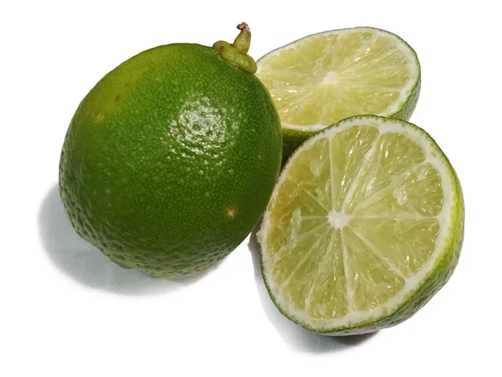 Un fruct verde, rotund, de lime, lângă două jumătăți cu miezul verde-pal, pe fond alb