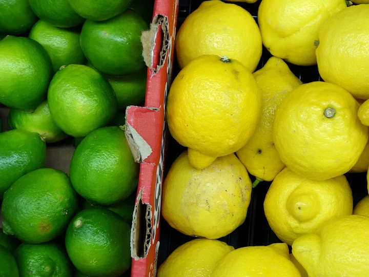 Lădițe cu lime verzi, la stânga, și lămâi galbene, la dreapta, despărțite de un carton roșu