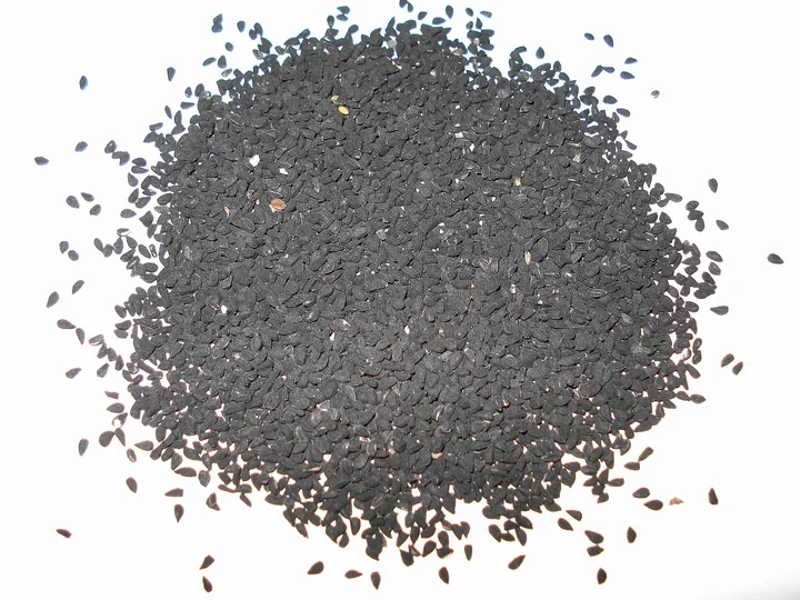 Grămadă de semințe mici, negre, de negrilică, pe un fond alb