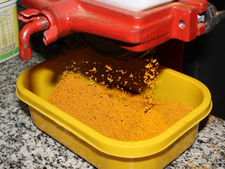 Pulbere de turmeric portocalie care cade dintr-o moară manuală roșie într-un vas galben