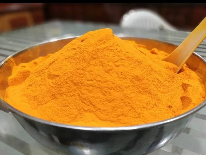 Pulbere fină de turmeric, portocalie, într-un castron de metal, cu o lingură de lemn