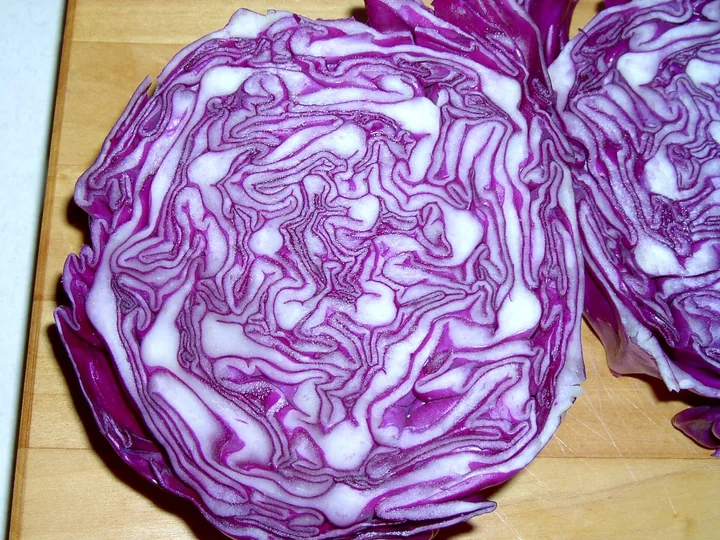 Căpățână de varză roșie tăiată în două, cu frunzele violet și albe răsucite una peste alta, pe un blat de lemn